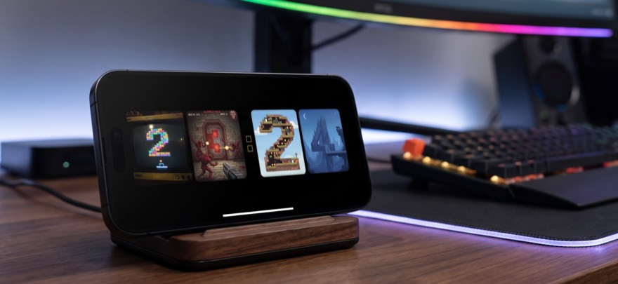 An iPhone on a wooden stand at a gaming desk, showing the time in retro video-game digits