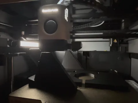 A 3D printer inside its enclosure, printing frame parts: a desk stand and a dock taking shape on the bed