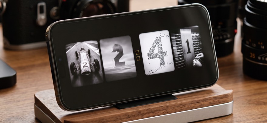 An iPhone on a walnut dock between vintage cameras, showing the time in black-and-white photographs